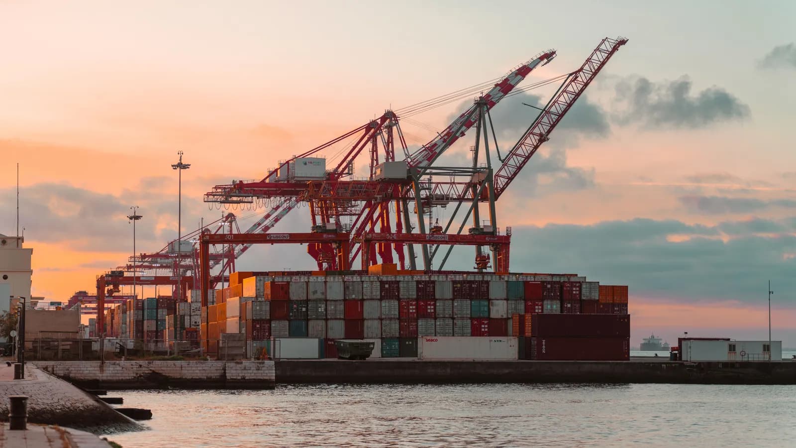 Porto de contêineres ao entardecer, com guindastes e um navio atracado no cais