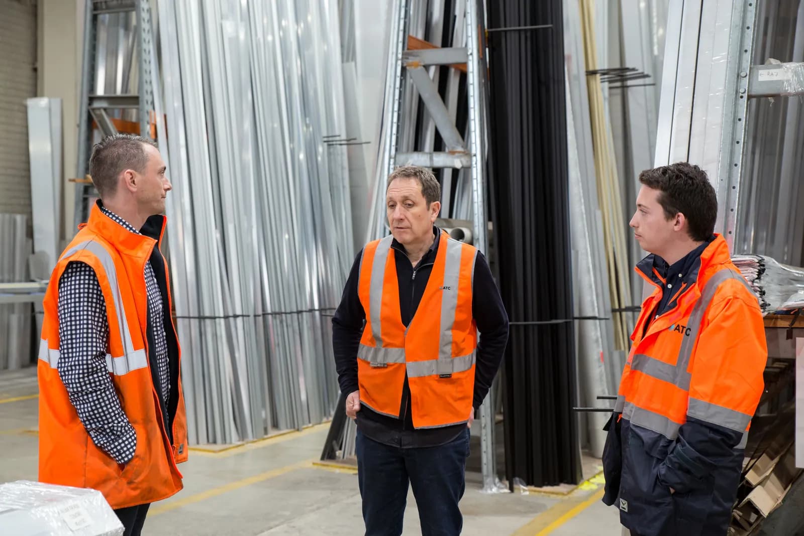 Equipe de armazém com coletes de segurança conversando sobre o trabalho em um galpão industrial